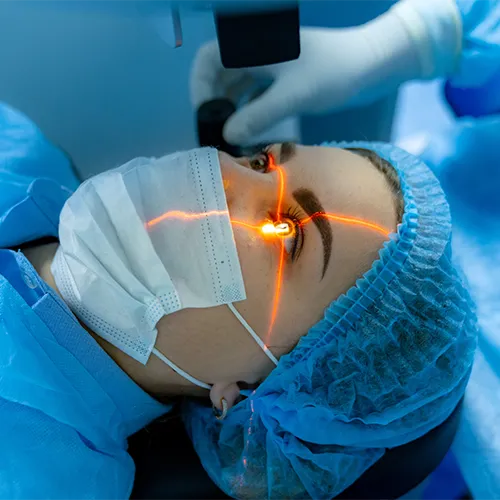 Paciente em sala cirúrgica realizando cirurgia refrativa com laser, sob campo estéril e máscara de proteção.