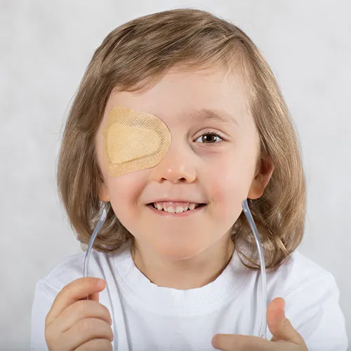 Criança sorridente usando tampão ocular infantil no olho direito, em tratamento para correção de ambliopia.
