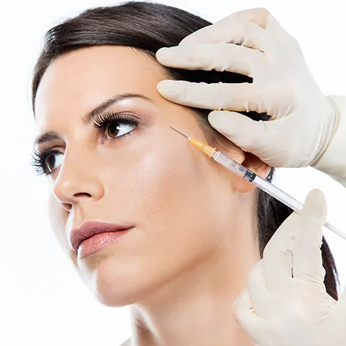 Mulher recebendo aplicação de toxina botulínica na região próxima aos olhos por profissional com luvas médicas.
