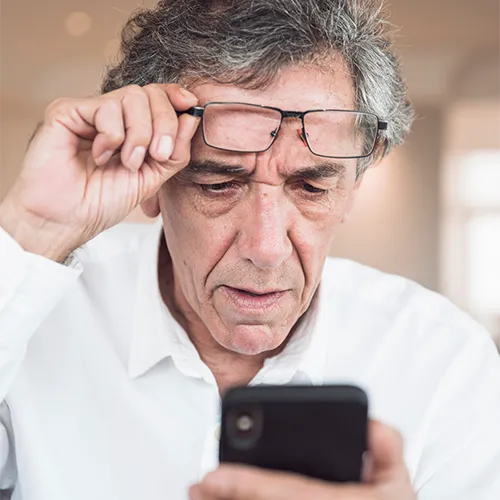 homem tirando os óculos para ler algo no smartphone, sinal de presbiopia